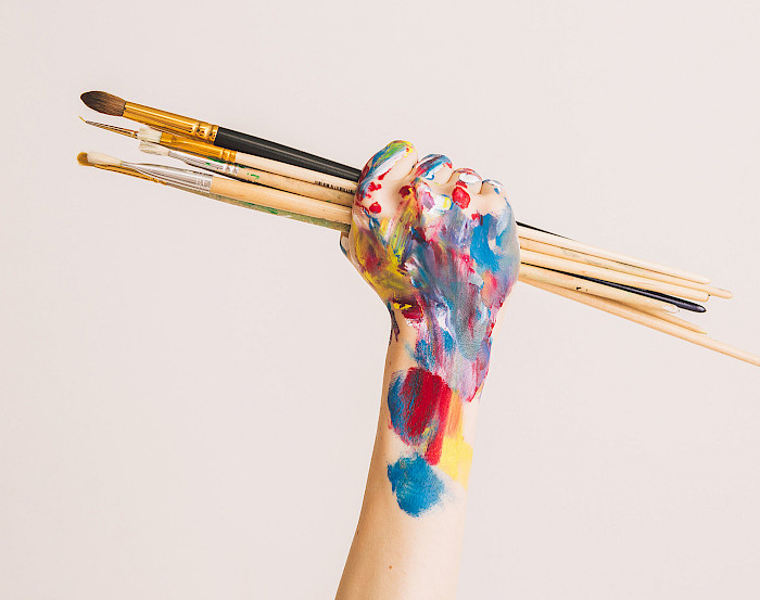 bunt bemalte Hand hält mehrere Malpinsel nach oben
