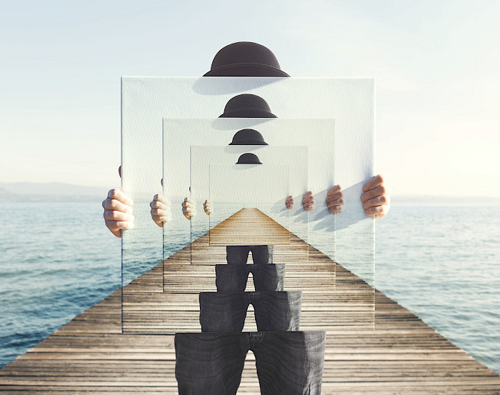 Mensch auf einem Steg ins Meer hält einen großen Spiegel in den Händen